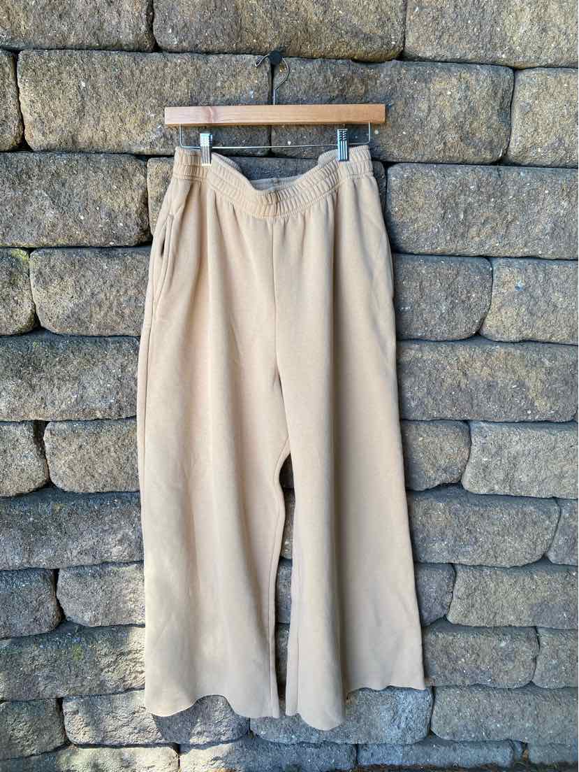 Tan wide-leg pants with a high waist and a loose, relaxed fit hanging on a wooden hanger.