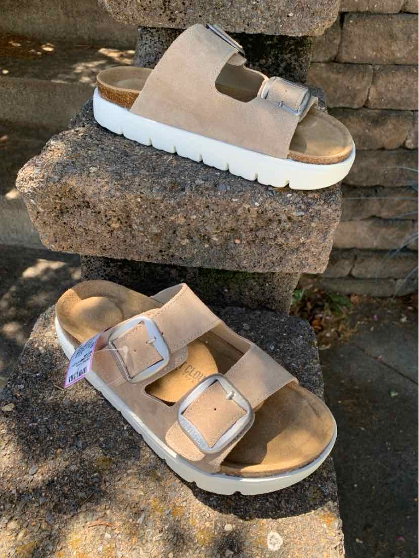 Beige sandal with two wide adjustable straps and silver buckles, cushioned footbed, thick white ridged sole.