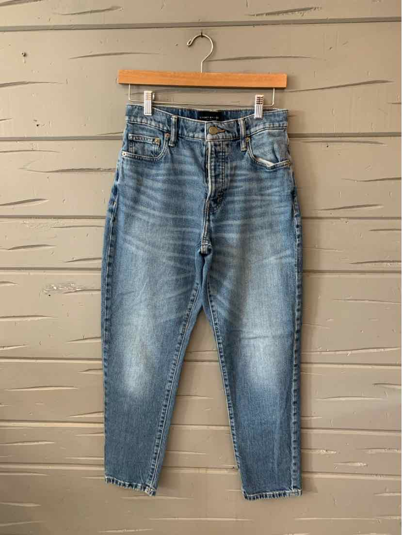 Blue high-waist Lucky Brand denim jeans with a tapered leg and frayed hems hanging on wooden hanger.