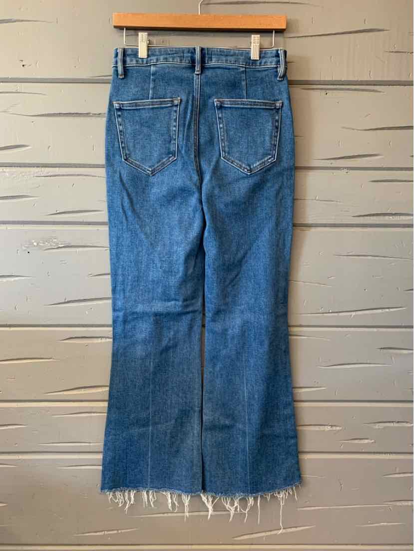 Blue denim jeans with frayed hem hanging on wooden hanger against textured wall, casual style for women's dresses and.