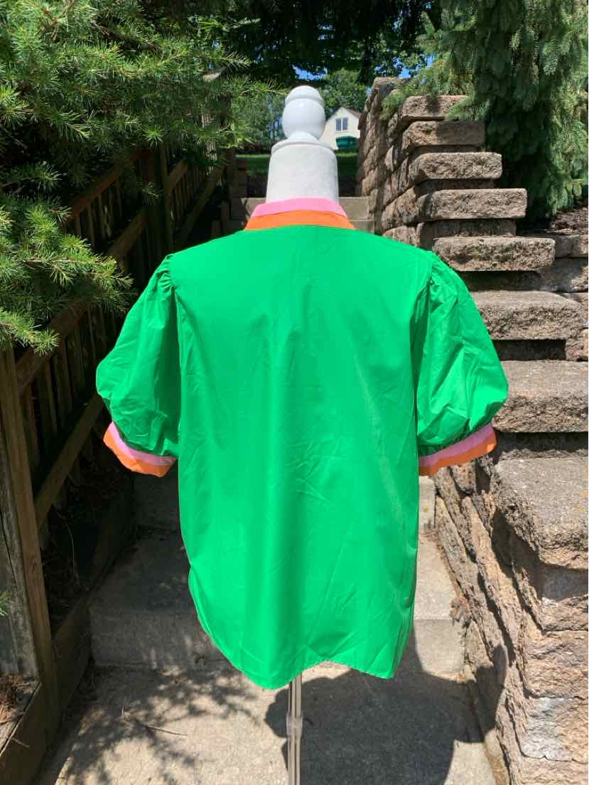 Bright green short-sleeve shirt with loose fit and straight hem on mannequin against outdoor stone and greenery background.