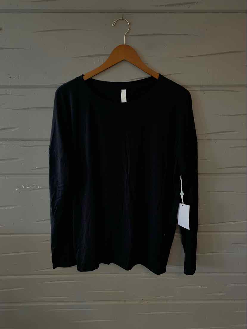 Black long-sleeve crewneck shirt in large size hanging on wooden hanger against gray wall.