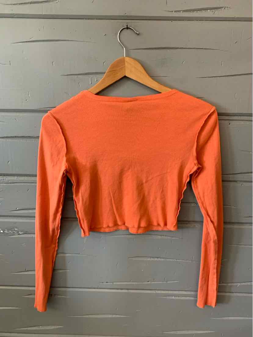 Orange long-sleeve cropped top with fitted silhouette hanging on wooden hanger against gray wooden background.