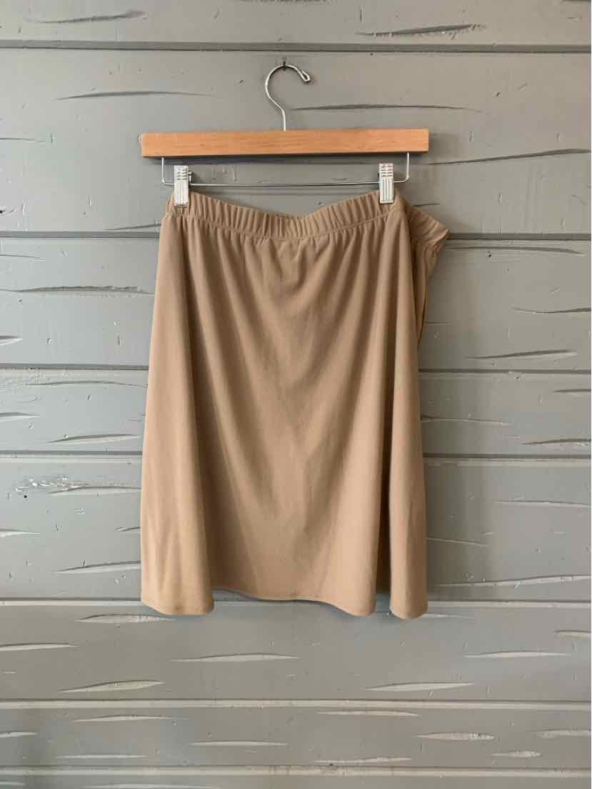 Beige knee-length skirt with elastic waistband hanging on wooden hanger against gray wooden wall.
