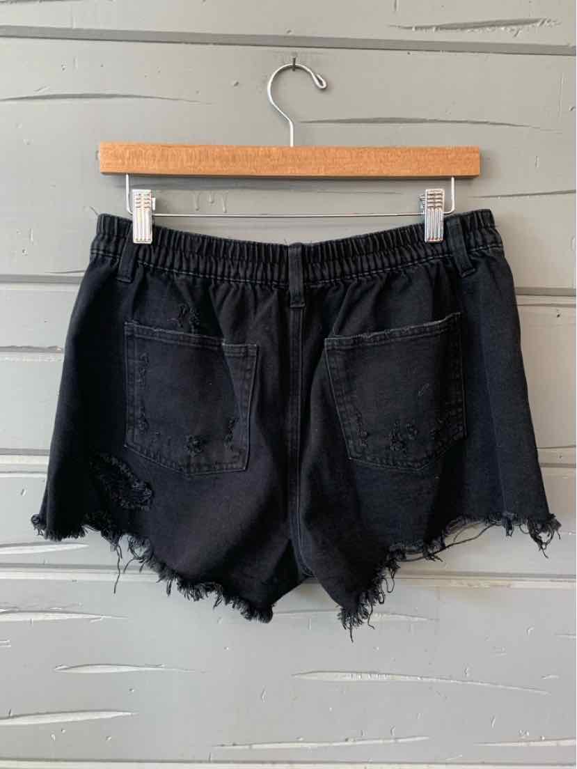 Black high-waisted denim shorts with frayed hems and two back pockets on a wooden hanger.