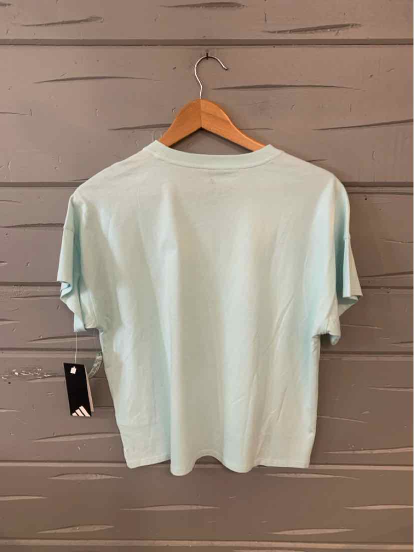 Light teal oversized Adidas T-shirt in XL with short sleeves hanging on wooden hanger against gray wooden wall.