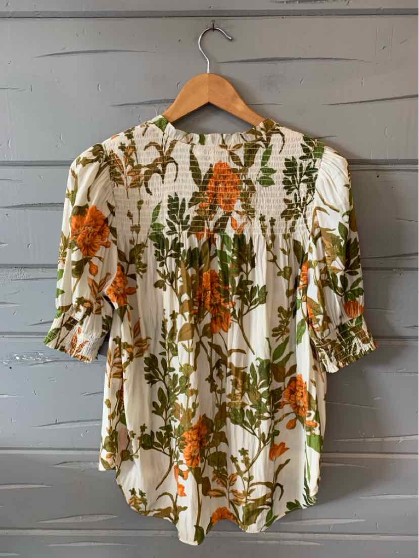 White blouse with green leaves and orange rose floral print, three-quarter sleeves, gathered details, and rounded hem.