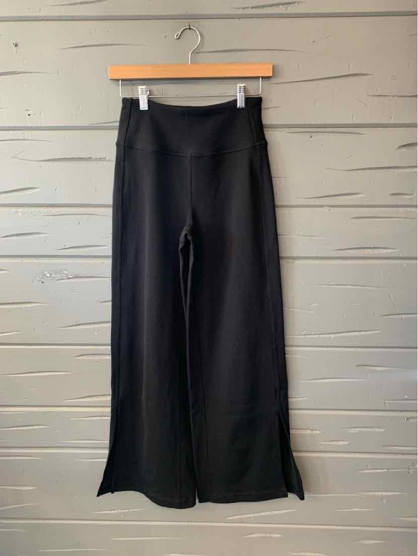 Black women’s wide-leg pants with a smooth finish and high-rise waistband, hanging on a wooden hanger.