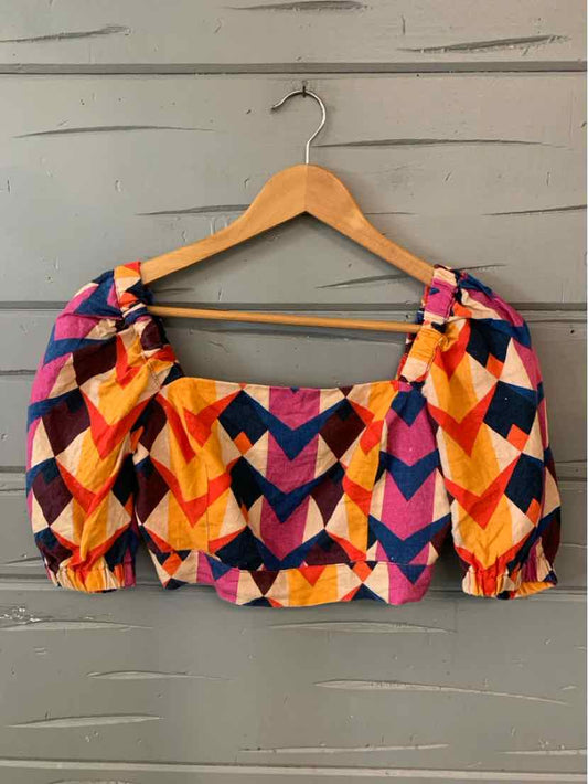 Colorful cropped blouse with puffed sleeves featuring geometric chevron pattern in orange, pink, purple, and black.