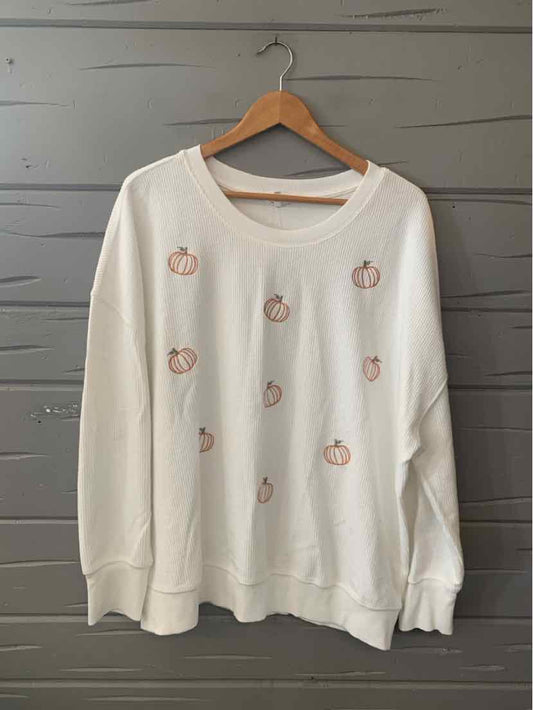 White oversized sweatshirt with small embroidered orange pumpkins scattered across the front.