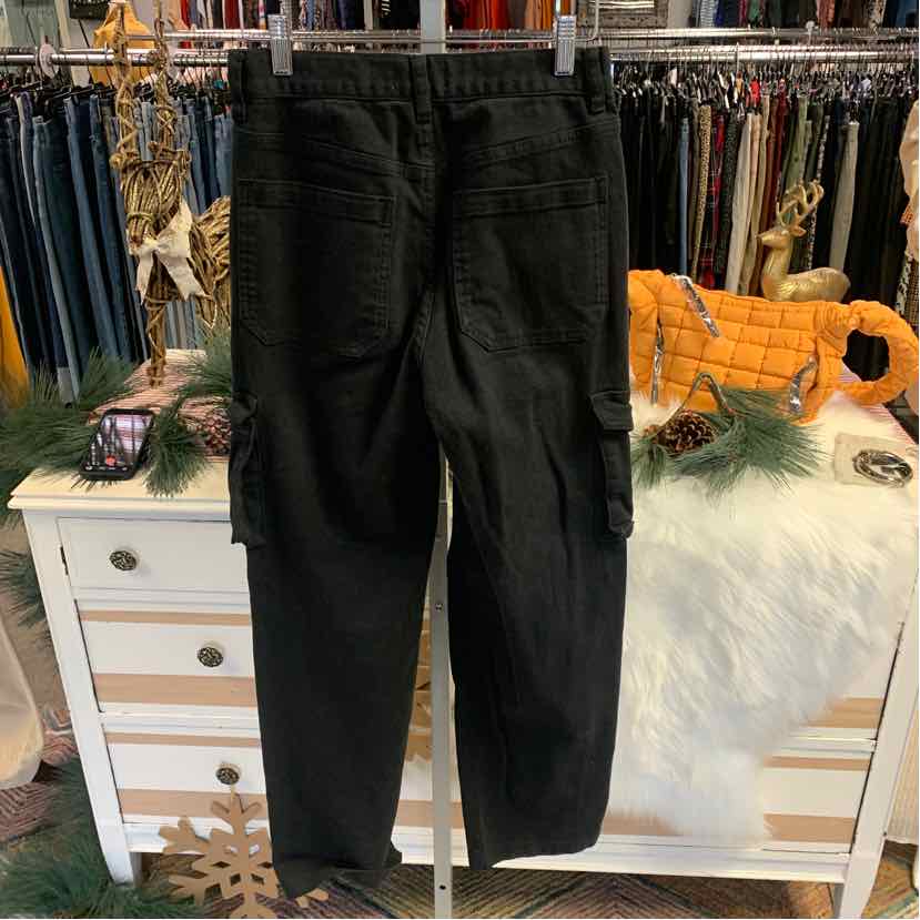 Black denim cargo pants with multiple pockets and a tapered fit hanging on a white dresser.