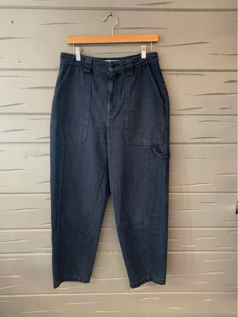 Black high-waisted trousers with front pleats and side pockets hanging on wooden hanger.
