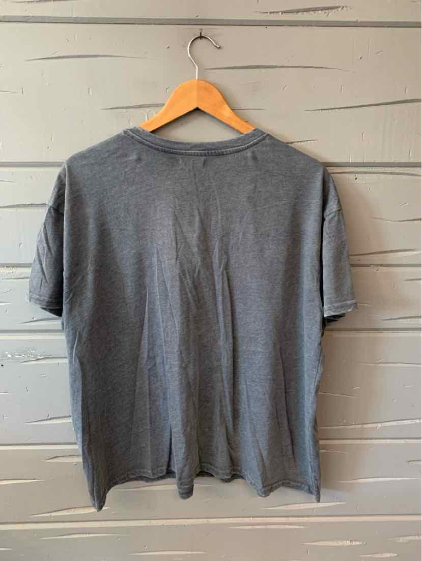 Gray short-sleeve t-shirt with crew neckline hanging on wooden hanger against gray wooden wall.