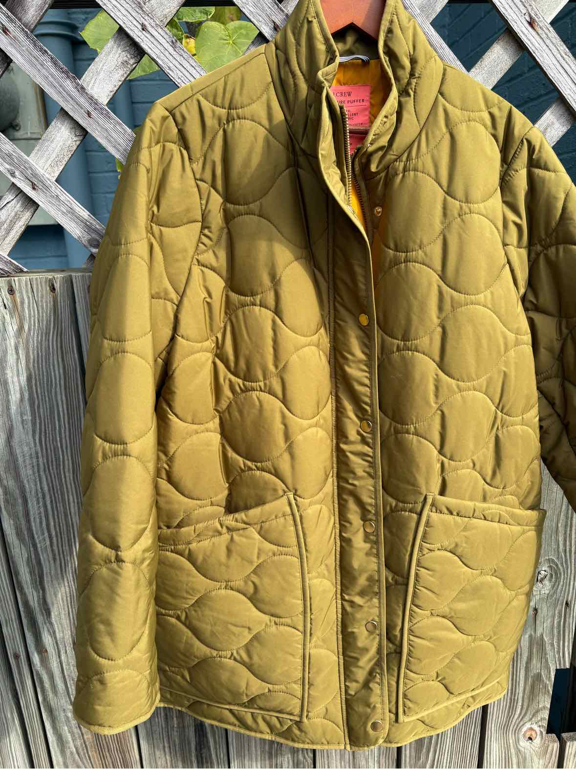 Olive green quilted women’s jacket with a stand collar, front pockets, and button closure.