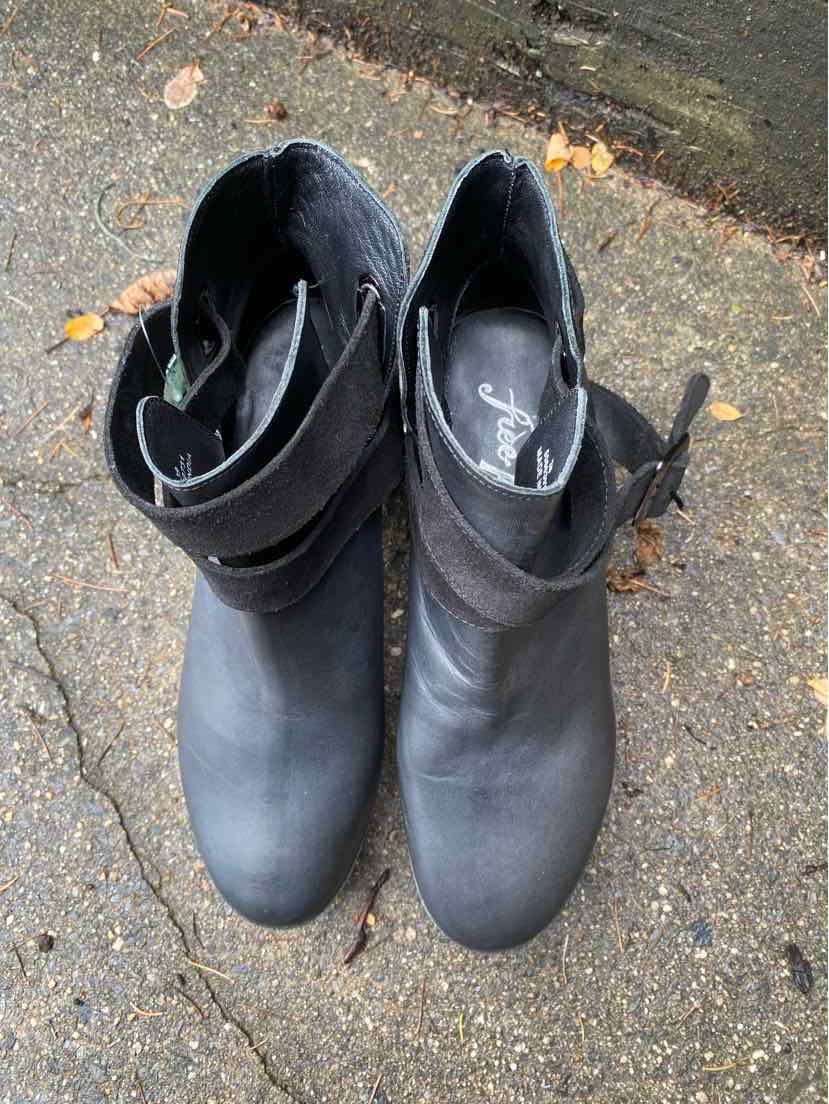 Black ankle boots with rounded toes, soft leather, side zipper, and a wrap-around ankle strap buckle detail.