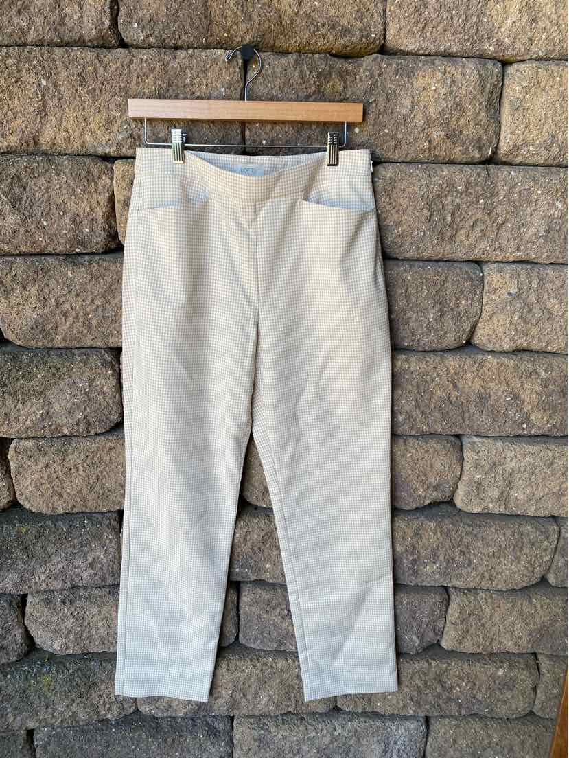Tan straight-leg pants with a mid-rise waist and side pockets, size 4, hanging against a stone wall background.