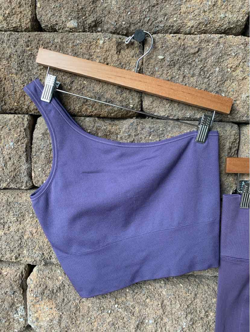 Purple one-shoulder cropped athletic top with ribbed texture hanging on wooden hanger.