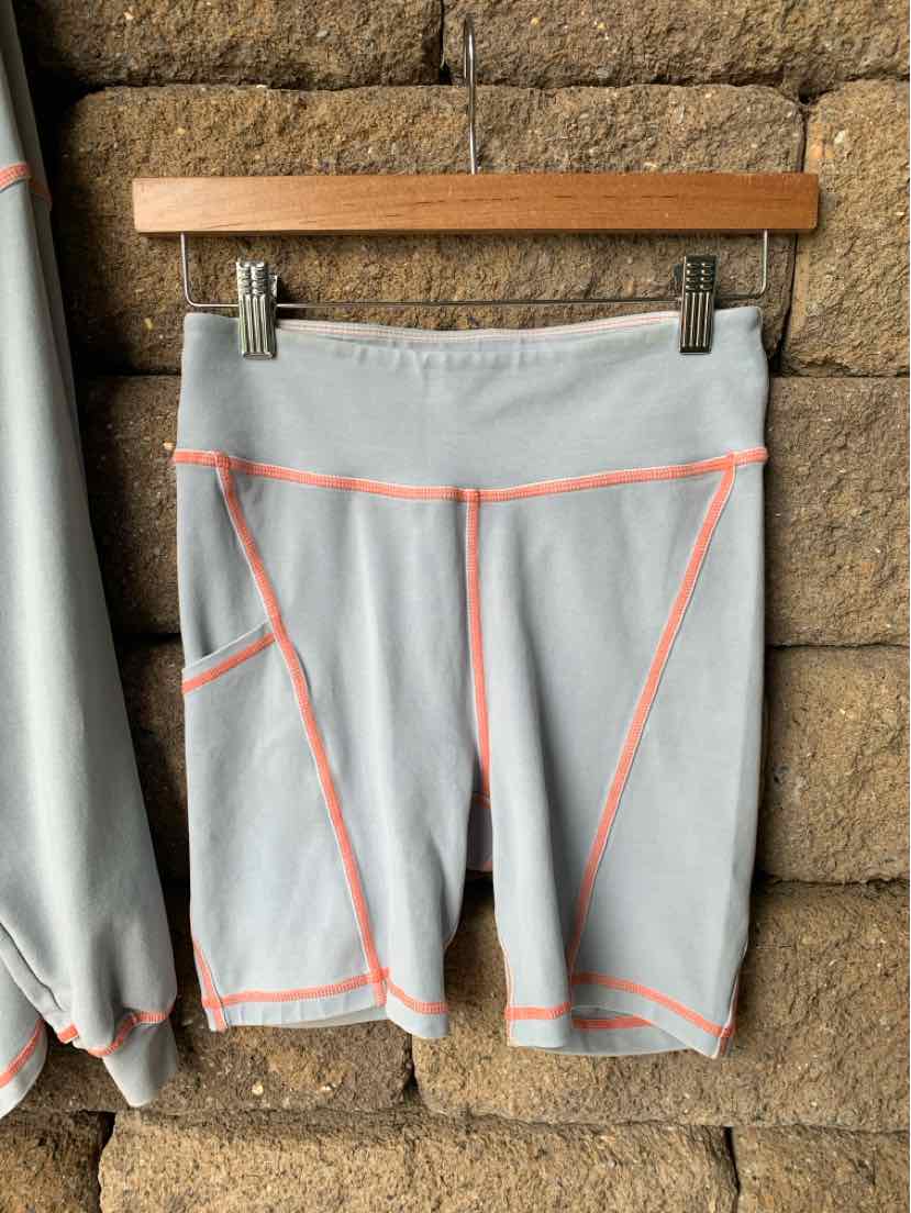 Light blue high-waist biker shorts with bright orange seam detailing and front pockets, hanging on wooden hanger.