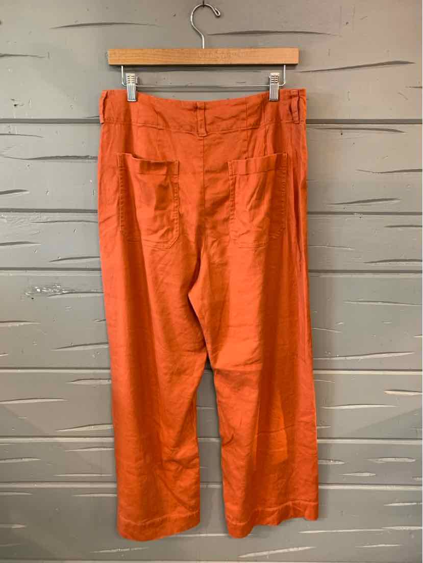 Orange high-waist pants with wide legs and a smooth, solid fabric hanging on a wooden hanger.