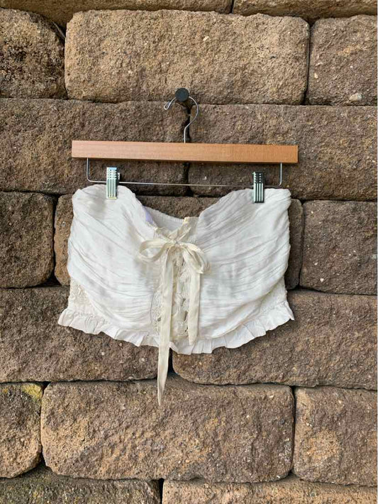 White cropped lace-up top with ruffled edges and lightweight fabric hanging on wooden hanger against stone wall.
