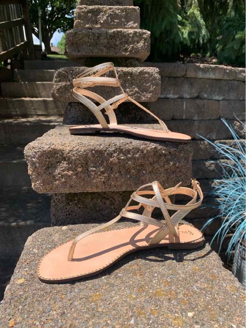 Beige strappy flat sandal with crisscross leather straps and a tan cushioned footbed.