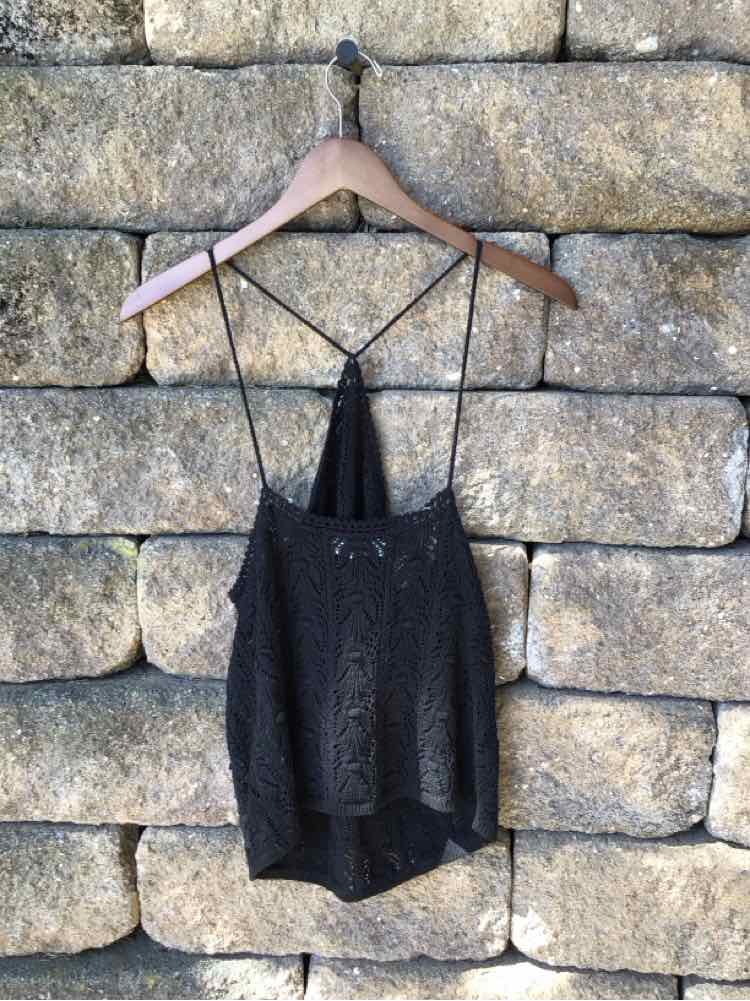 Black crochet sleeveless top with thin straps and scalloped hem hanging on wooden hanger.
