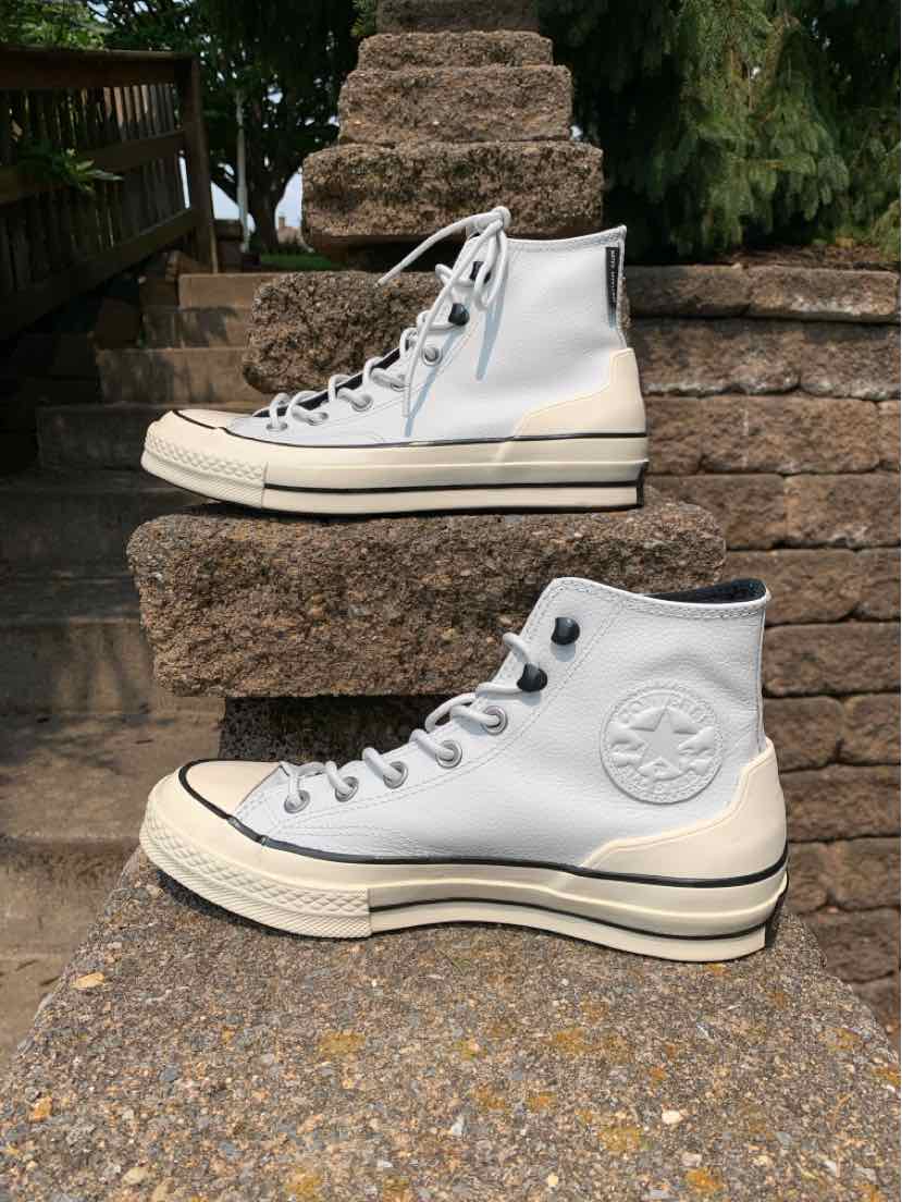 White high-top Converse sneakers with black stripe detailing on thick rubber soles and white laces.