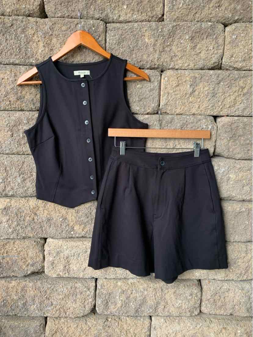 Black sleeveless button-up vest with collar and matching high-waist shorts with front pleats.