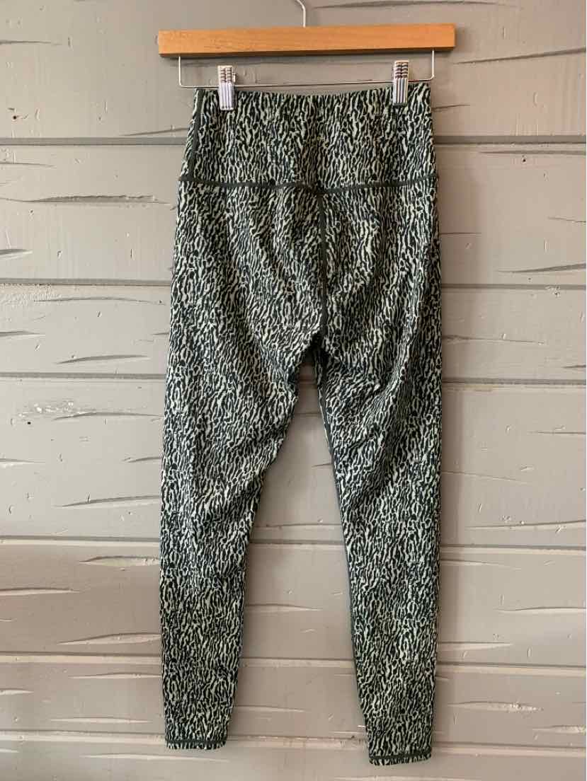 Green cheetah print leggings with high waist and slim fit hanging on wooden hanger against wooden wall.