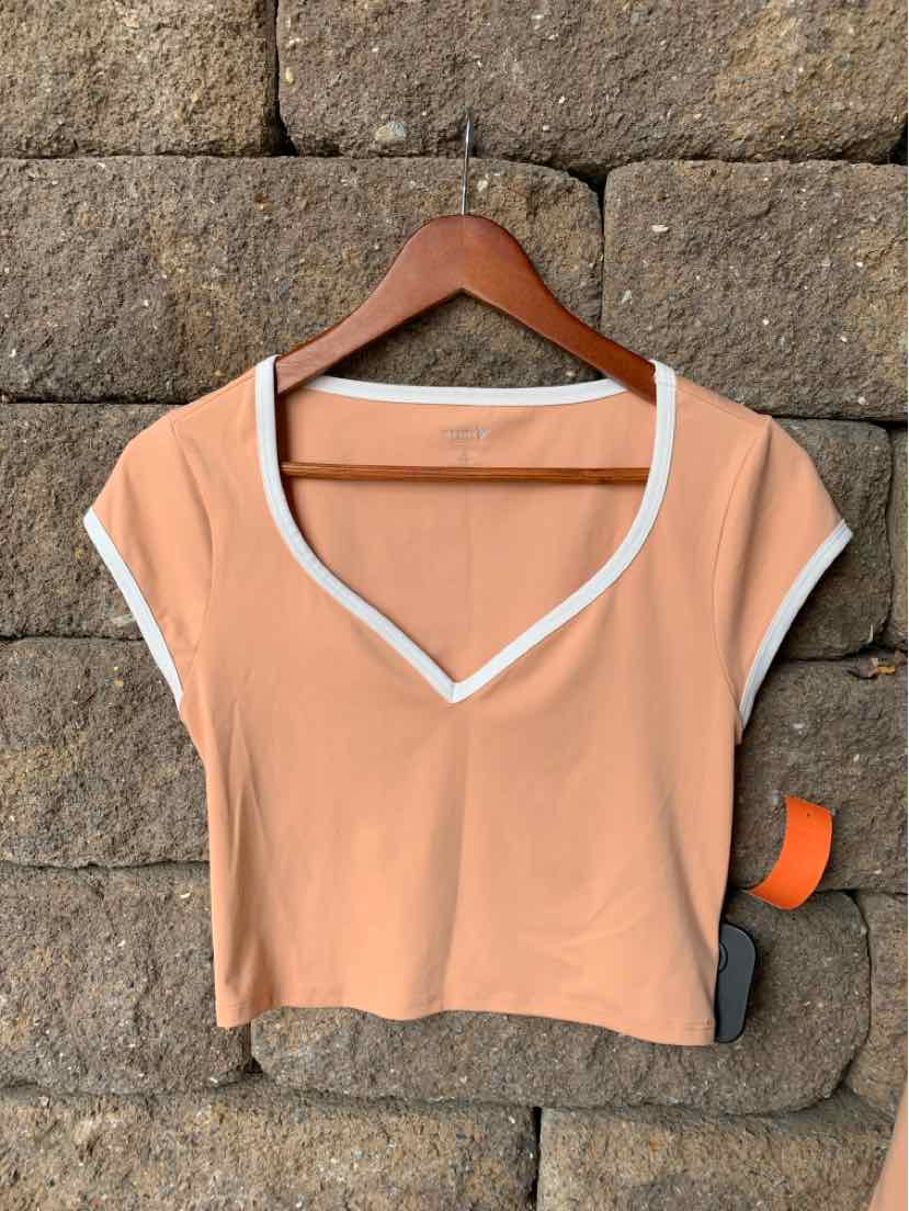 Peach cropped active top with white trim, short sleeves, and V-neck collar.