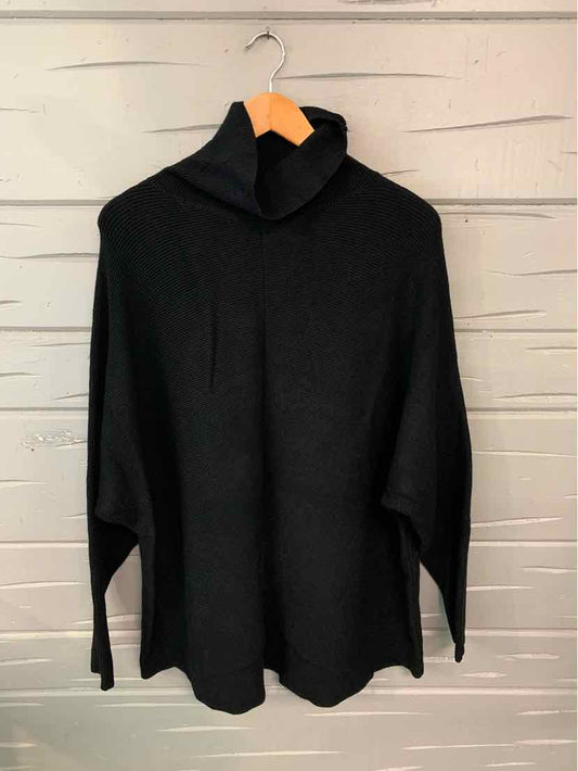 Black oversized turtleneck sweater with wide sleeves hanging on wooden hanger.
