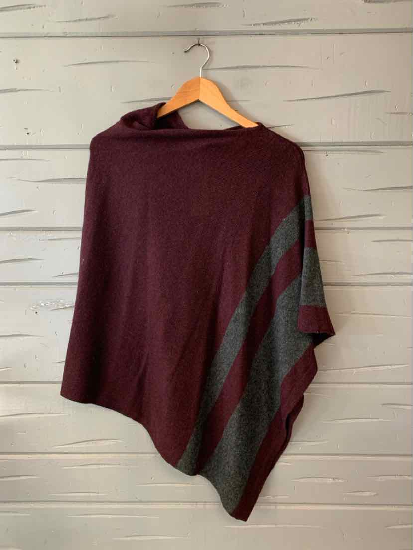 Burgundy knit poncho with dark gray diagonal stripes and asymmetrical hem on wooden hanger.