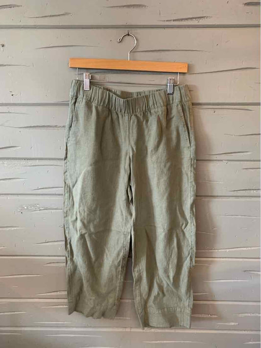 Olive green cropped pants with elastic waistband and side pockets on wooden hanger.