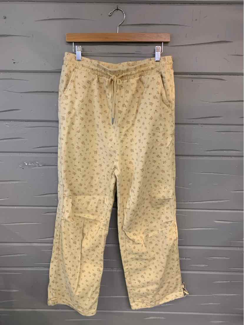 Beige medium pants with a small dark floral print and a drawstring waist hanging on a wooden hanger.