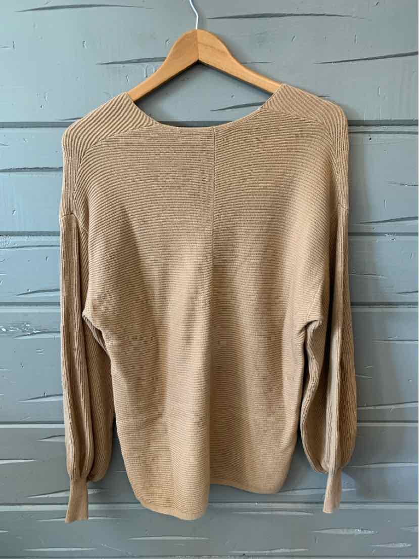 Tan long-sleeve knit sweater with ribbed cuffs and crew neckline hanging on wooden hanger.