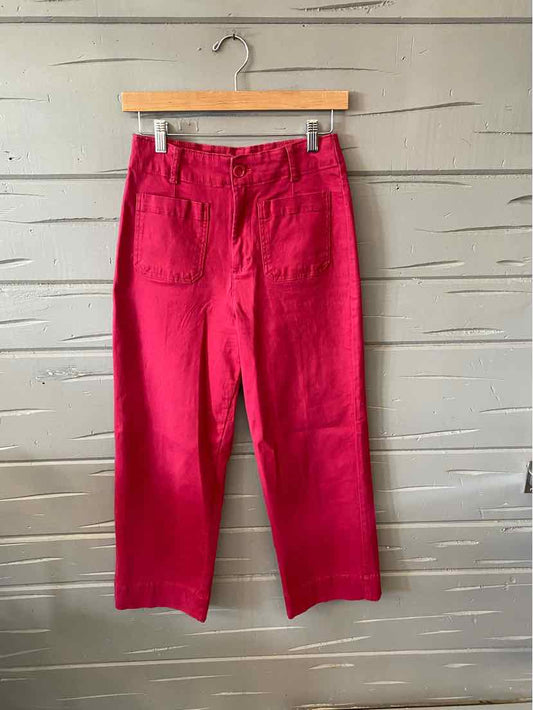 Bright red straight-leg pants with front patch pockets and a high waist on a wooden hanger.