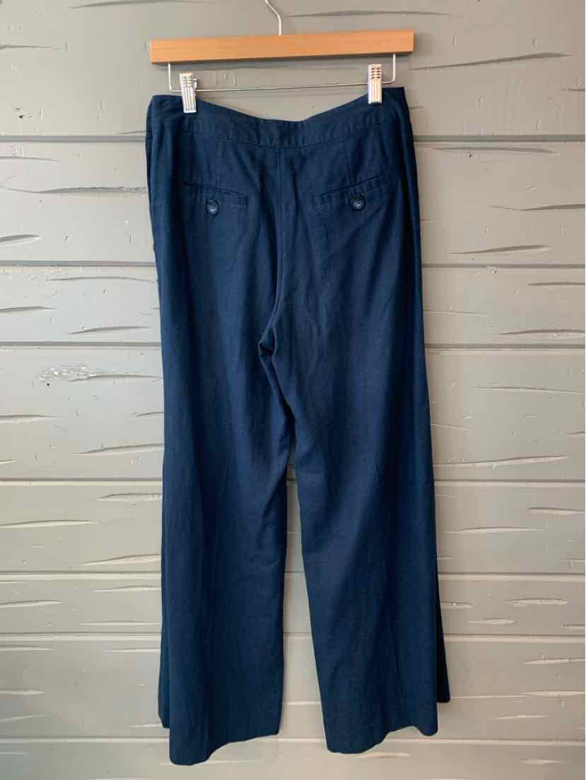 Navy blue wide-leg pants with back button flap pockets and tailored waistband hanging on wooden hanger.