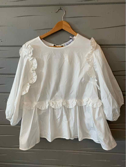 White long-sleeve blouse with ruffled detailing along shoulders and waist, loose fit, round neckline.