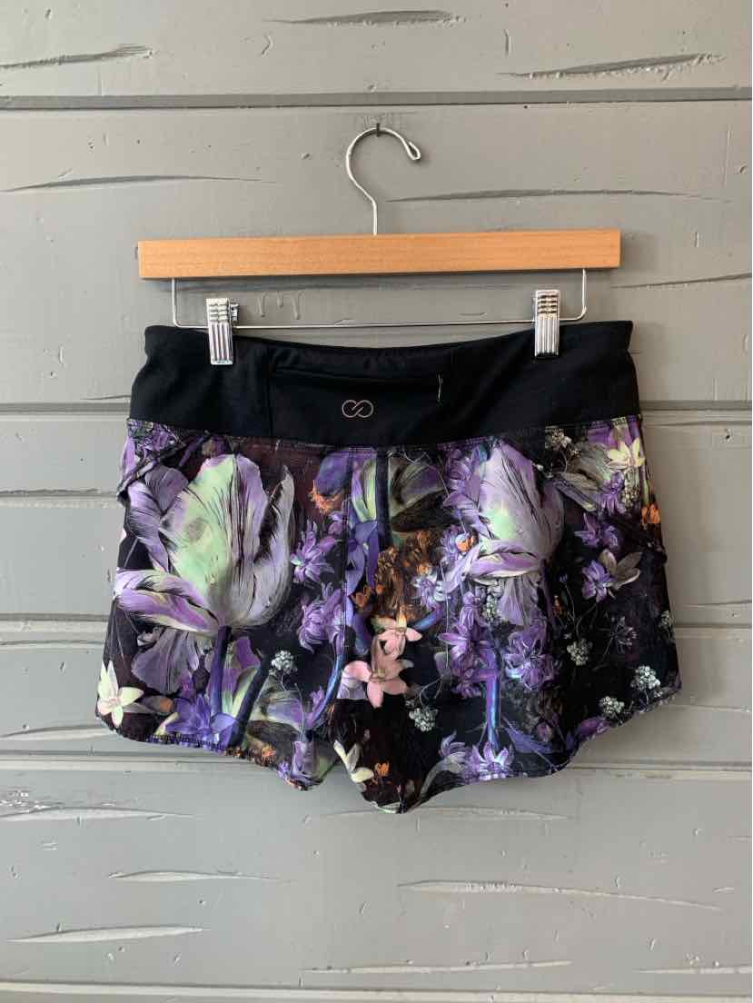 Women's athletic shorts with a black wide waistband and purple, lavender, and green floral print on a black background.