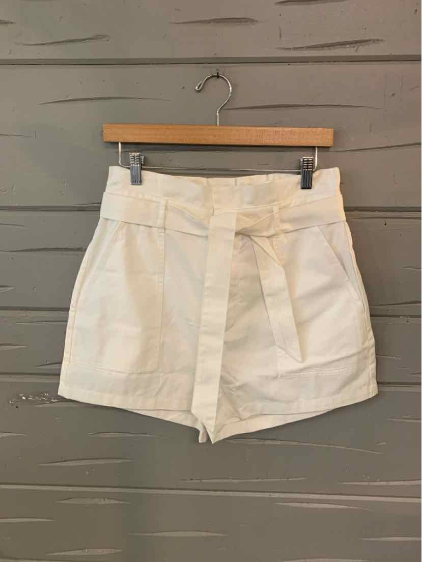 White high-waist shorts with fabric belt and front pockets on wooden hanger.