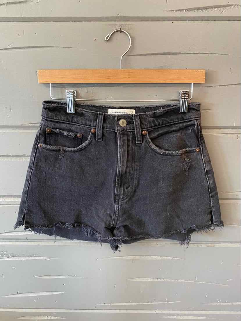 Black high-waisted denim shorts with frayed hem and button closure hanging on wooden hanger.