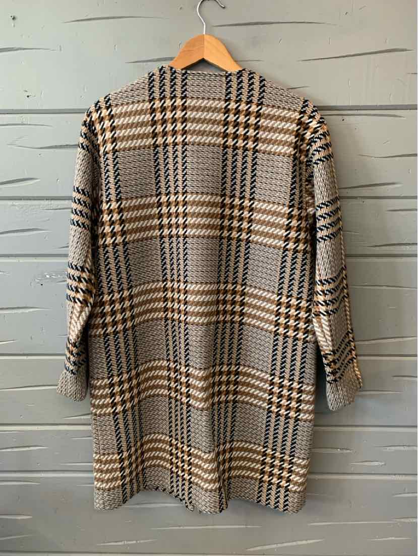 Long plaid coat in beige, black, and white with a straight silhouette and long sleeves hanging on a wooden hanger against a.