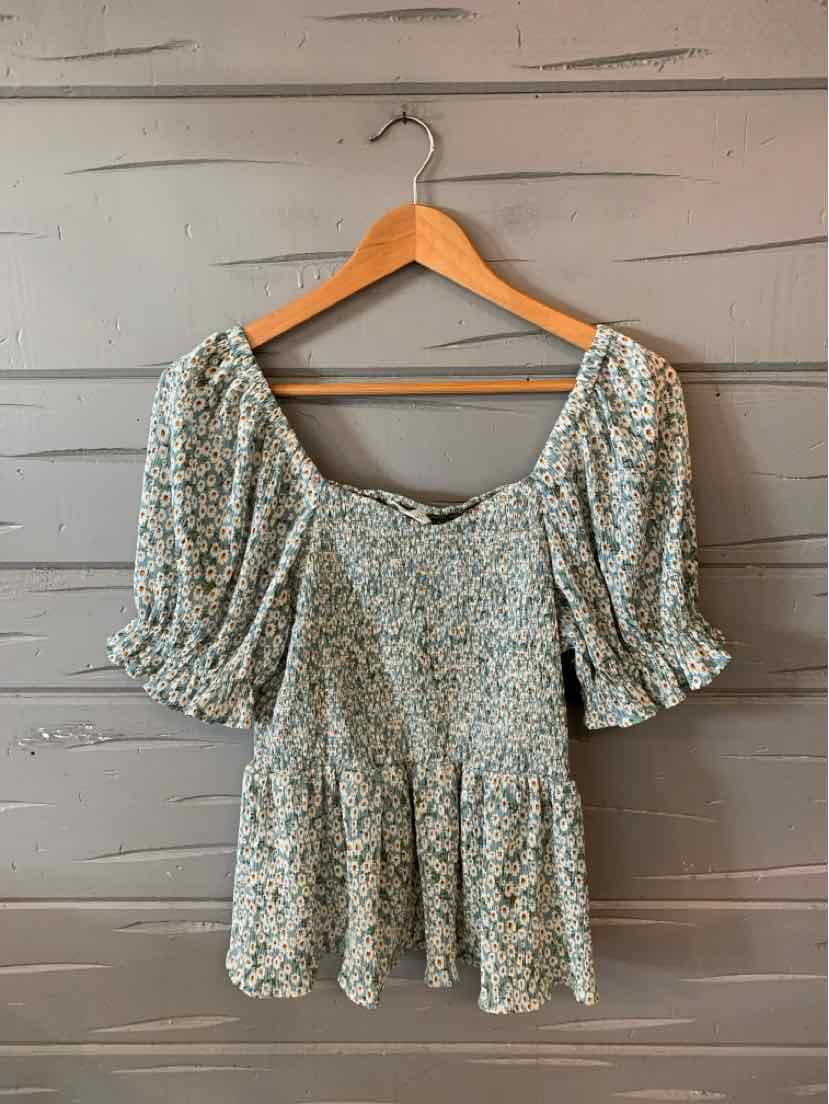Light green floral blouse with puff sleeves and ruched detailing on wooden hanger.