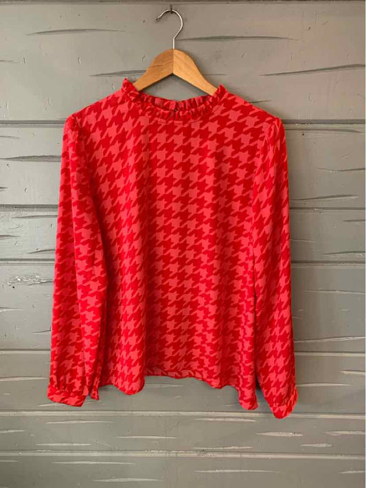 Red houndstooth long-sleeve blouse with round neckline and relaxed fit on wooden hanger.
