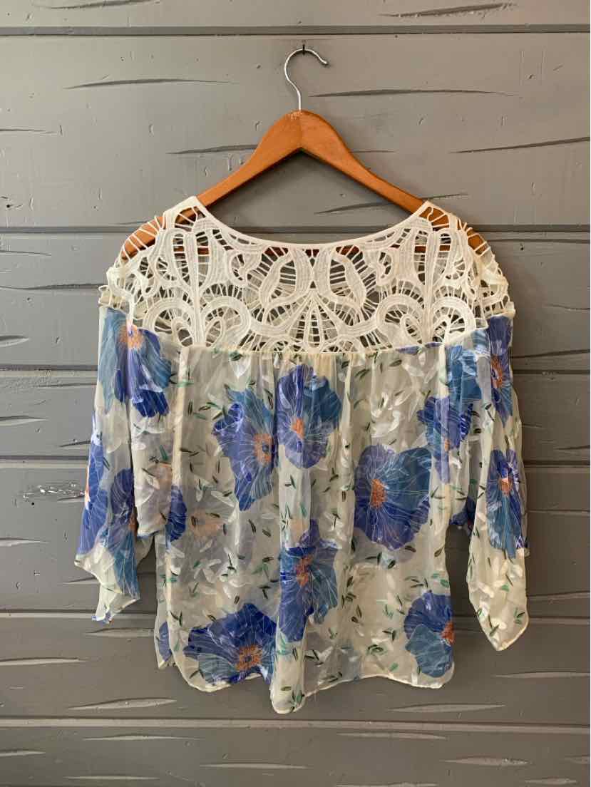 White blouse with blue floral print, loose fit, and intricate crochet lace yoke on top.
