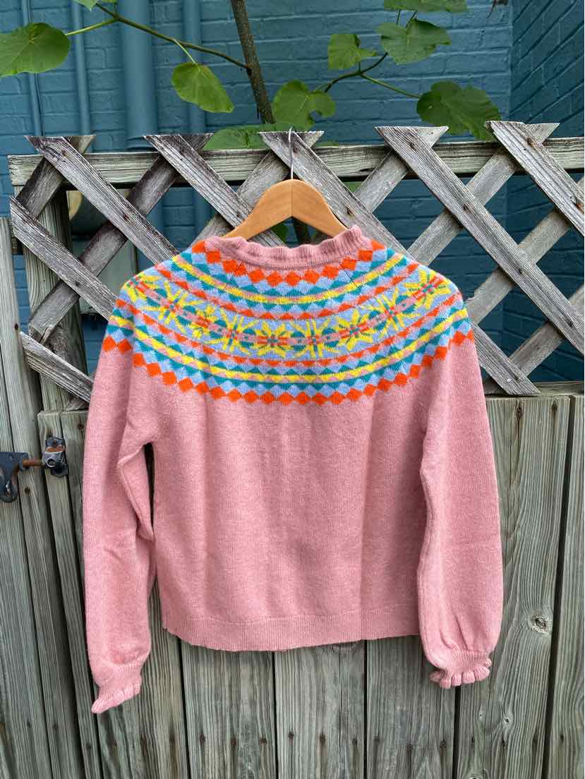 Pink knitted sweater with a colorful patterned yoke in blue, yellow, and orange, featuring long sleeves and ribbed cuffs.
