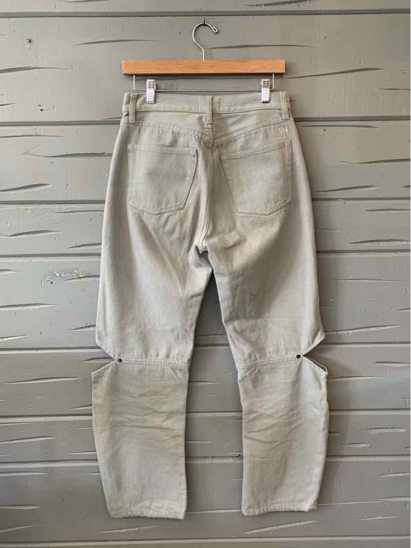 Light grey denim jeans with high waist, straight leg, and two back pockets hanging on wooden hanger against gray wooden wall.