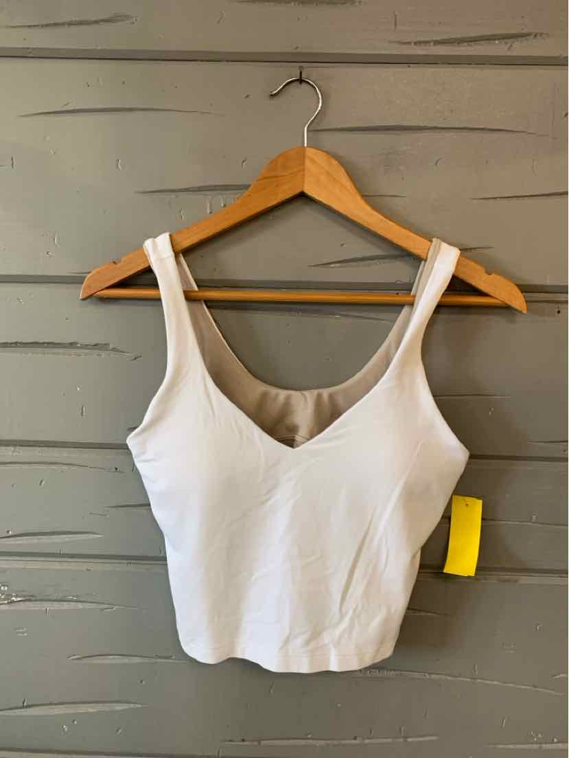 White sleeveless crop top with wide straps and a scoop neckline hanging on wooden hanger against gray wall.
