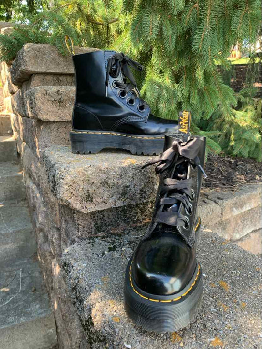 Shiny black leather Dr. Martens combat boots with thick platform soles, yellow stitching, and lace-up fronts.