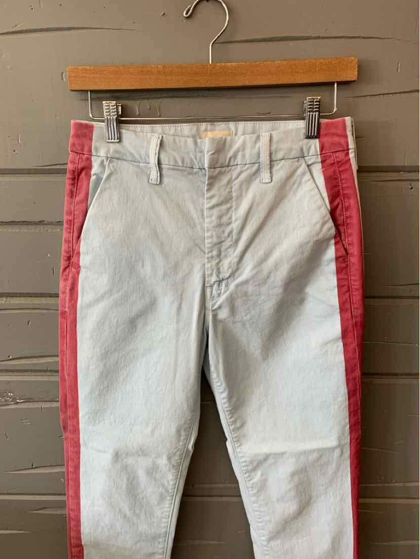 White trousers with coral pink side stripes hanging on wooden hanger against gray wall.